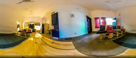 Una habitación con un tobogán de madera curvada, un ventilador de techo y vista hacia una zona de cocina con estantes y un refrigerador.