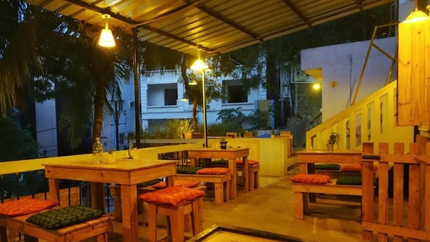 An outdoor seating area with wooden tables and chairs, a central coffee table, and hanging lights. - Shepherd Stories - Hostel (Hyderabad)