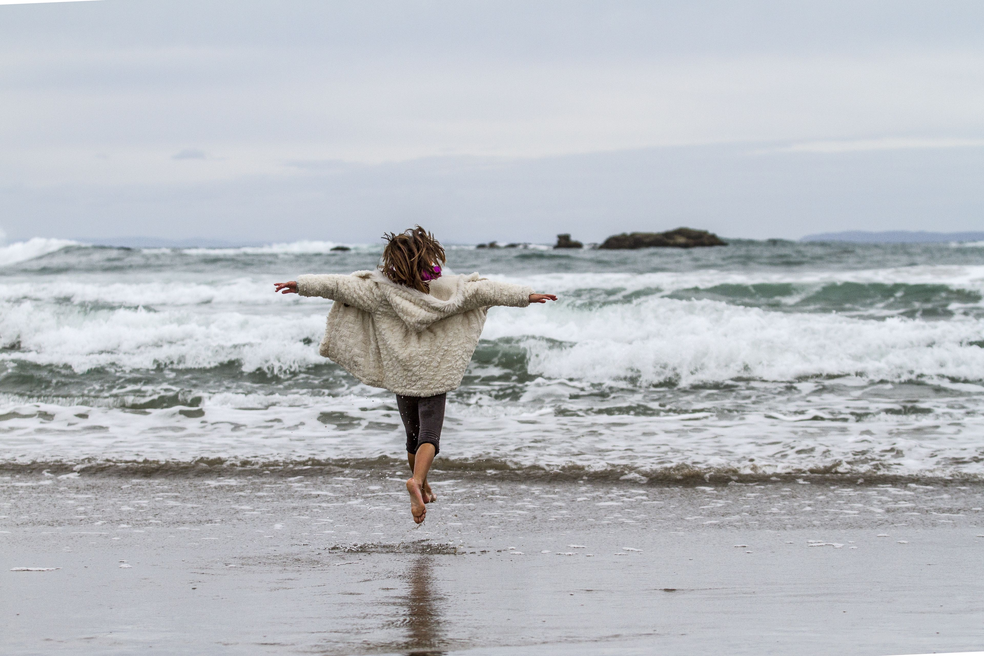 Une personne qui saute sur une plage, avec des vagues en arrière-plan.