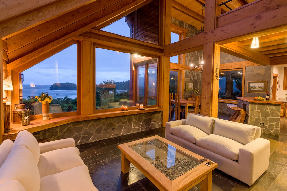 Un intérieur chaleureux avec une cheminée en pierre, un plafond en bois et une grande fenêtre donnant sur la mer.
