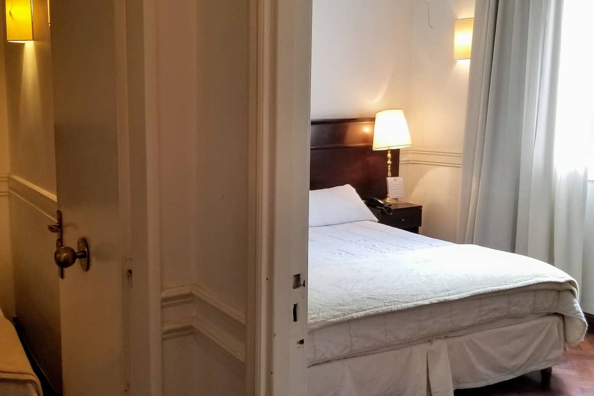 Ein Hotelzimmer mit einem Bett, einem Nachttisch mit Lampe und einer Tür zu einem weiteren Raum.