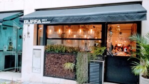 A restaurant with a black awning, glass doors, and a visible interior with hanging lights and plants. - Hotel San Antonio (Buenos Aires)