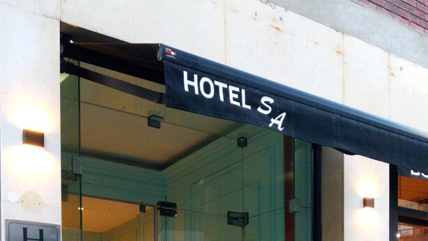 A hotel entrance with a glass door, a sign above the door, and a number on the wall. - Hotel San Antonio (Buenos Aires)
