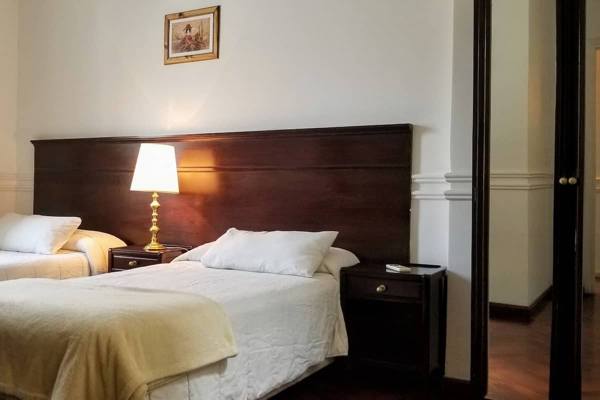Ein Hotelzimmer mit zwei Betten, einem Nachttisch mit Lampe, einem Schminktisch und einem gerahmten Bild an der Wand.
