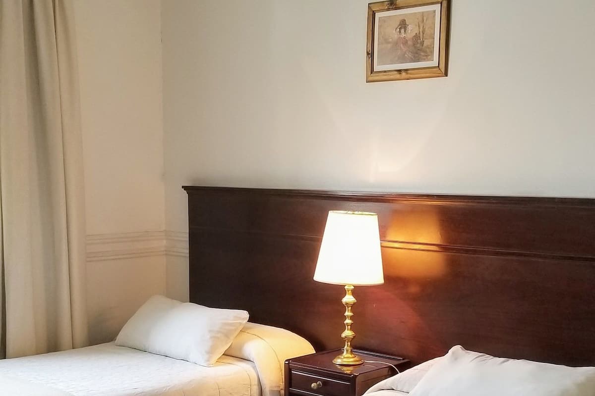 Ein Hotelzimmer mit zwei Betten, einem Holzkopfteil, einem Nachttisch mit Lampe und einem gerahmten Bild an der Wand.