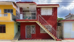 A two-story building with a red exterior, a balcony with metal railings, and a staircase leading to the upper floor. - Hostal MJ (Trinidad)