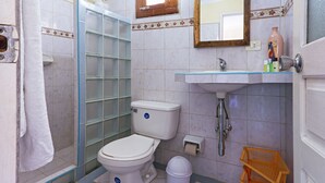 A bathroom with a toilet, a glass shower enclosure, a sink, and a mirror. - Hostal MJ (Trinidad)