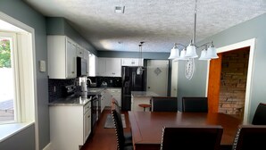 Een moderne keuken met witte kasten, een centraal eiland en een eethoek met een houten tafel en stoelen.