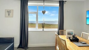 Una habitación con una mesa de comedor, sillas, un sofá, un ventanal con cortinas, un ventilador de techo y un cuadro en la pared.