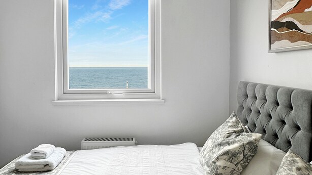 Un dormitorio con una cama grande, una ventana con vista al mar, un ventilador de techo y una obra de arte enmarcada en la pared.