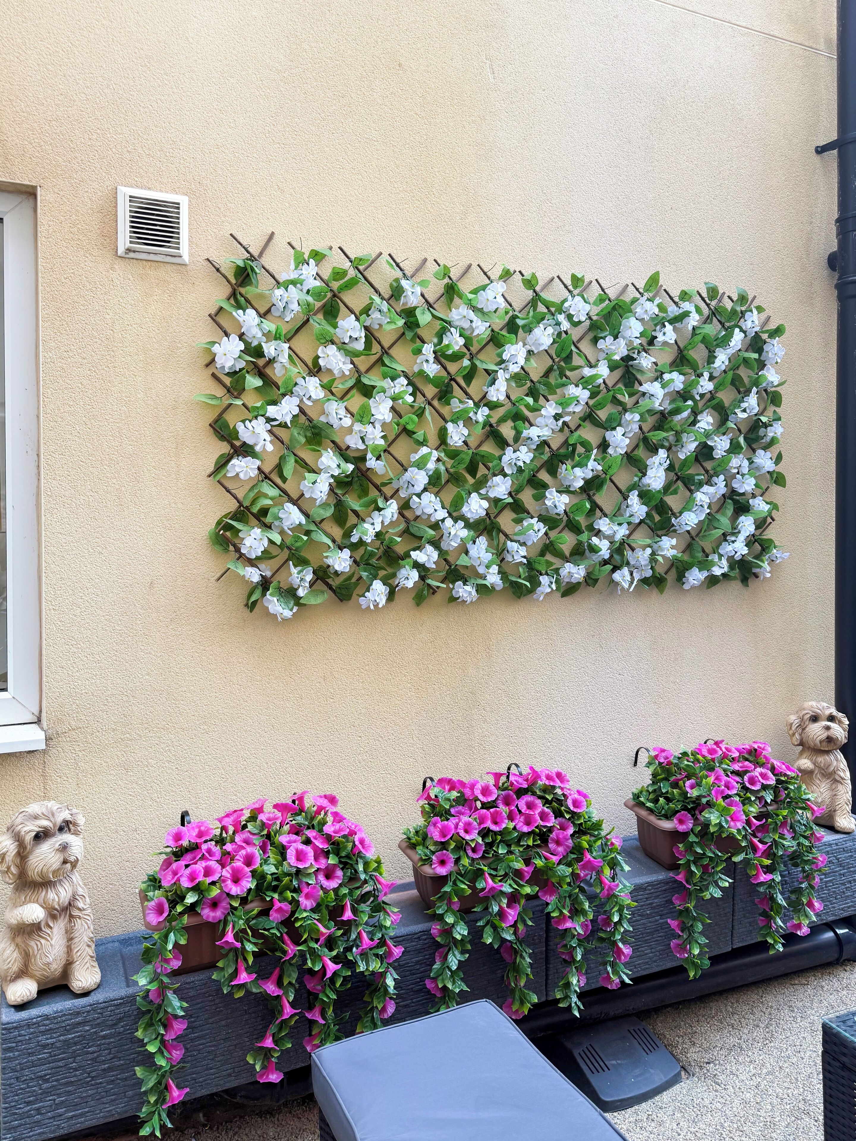 A wall-mounted flower grid with white flowers and a row of potted pink flowers below.