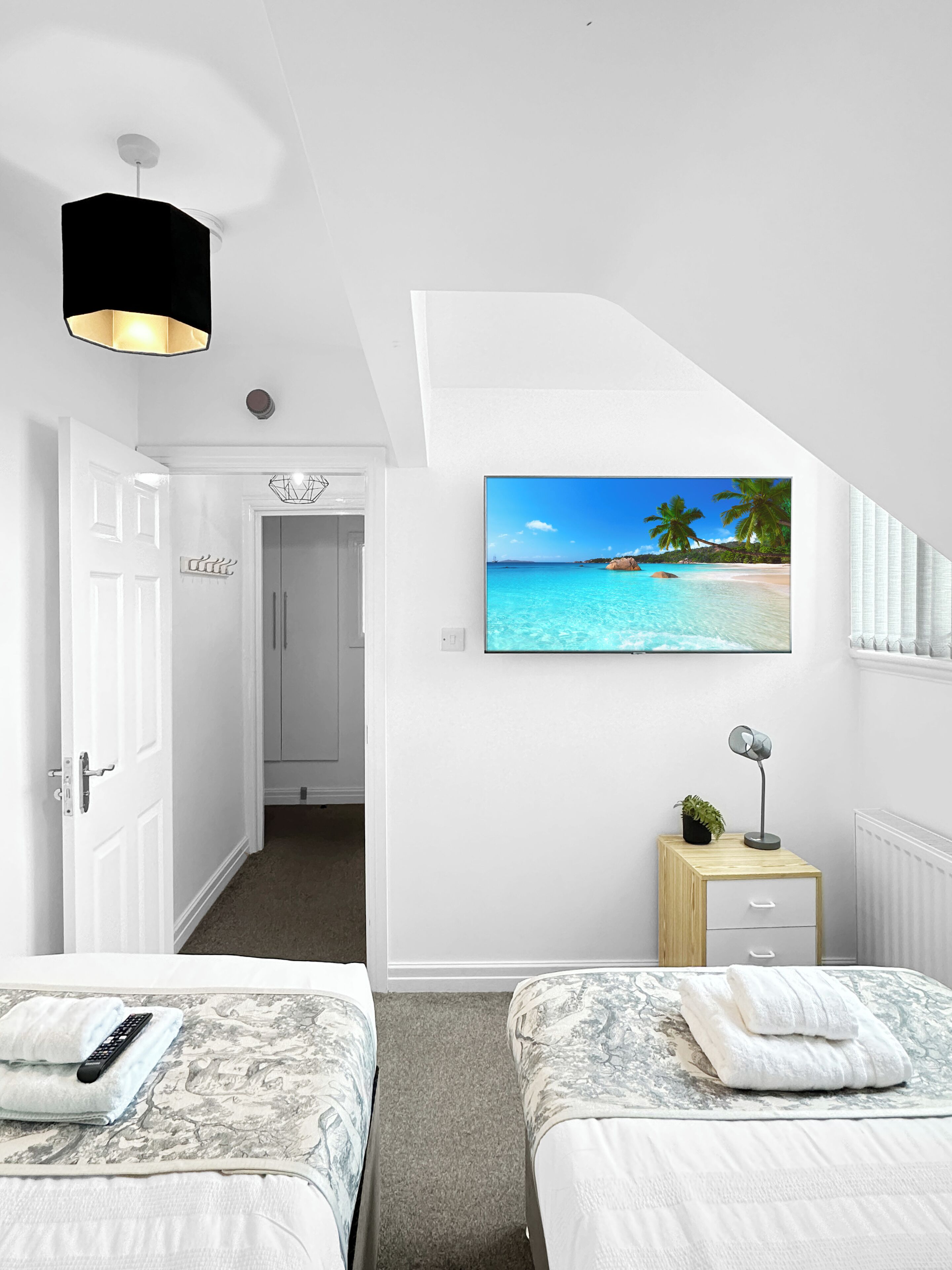 A bedroom with two beds, a TV on the wall, a small bedside table, and a door leading to another room.