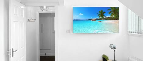 A bedroom with two beds, a TV on the wall, a small bedside table, and a door leading to another room.