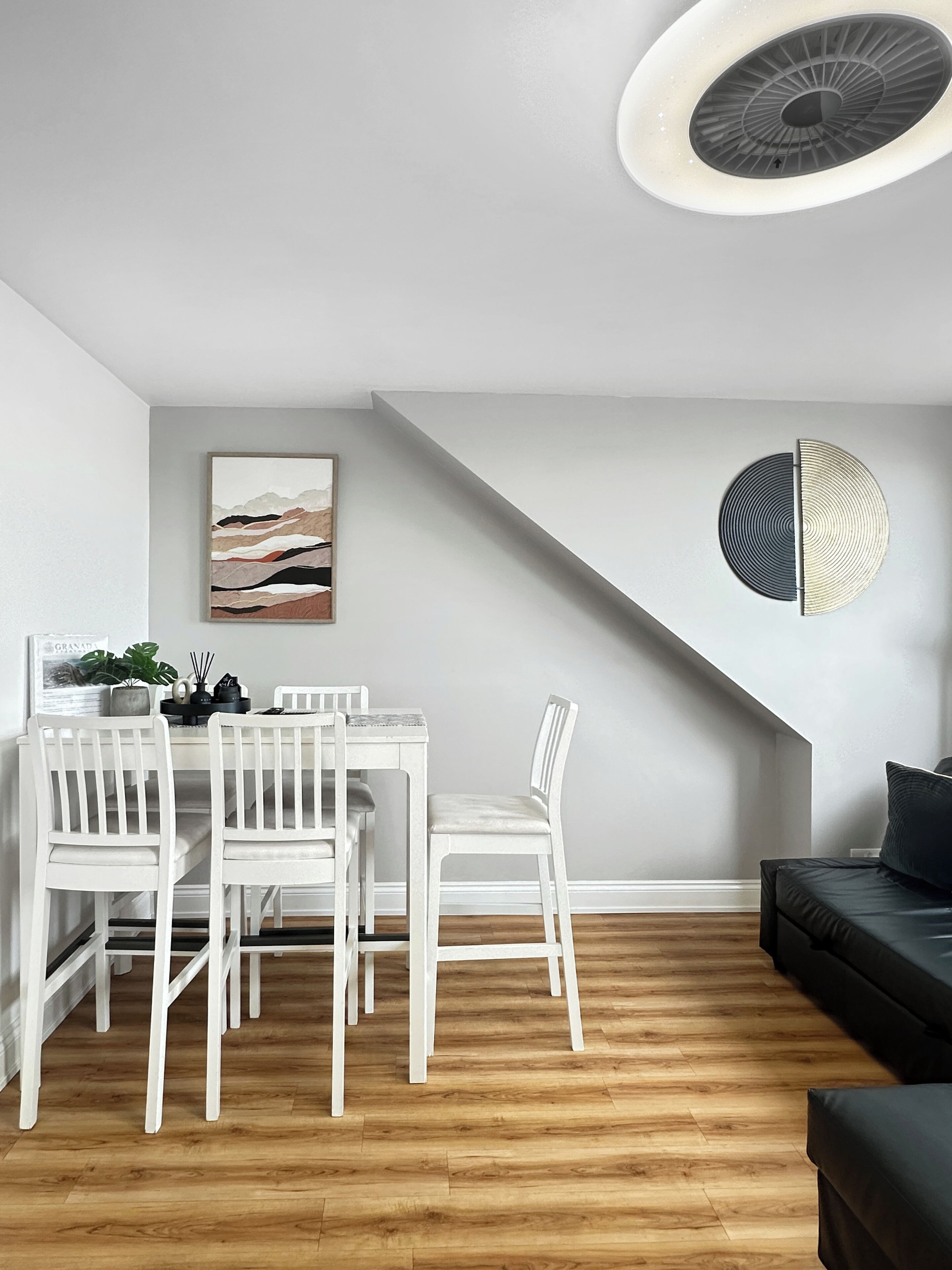 A modern dining area with white chairs and a table, a black sofa, and a ceiling light fixture.