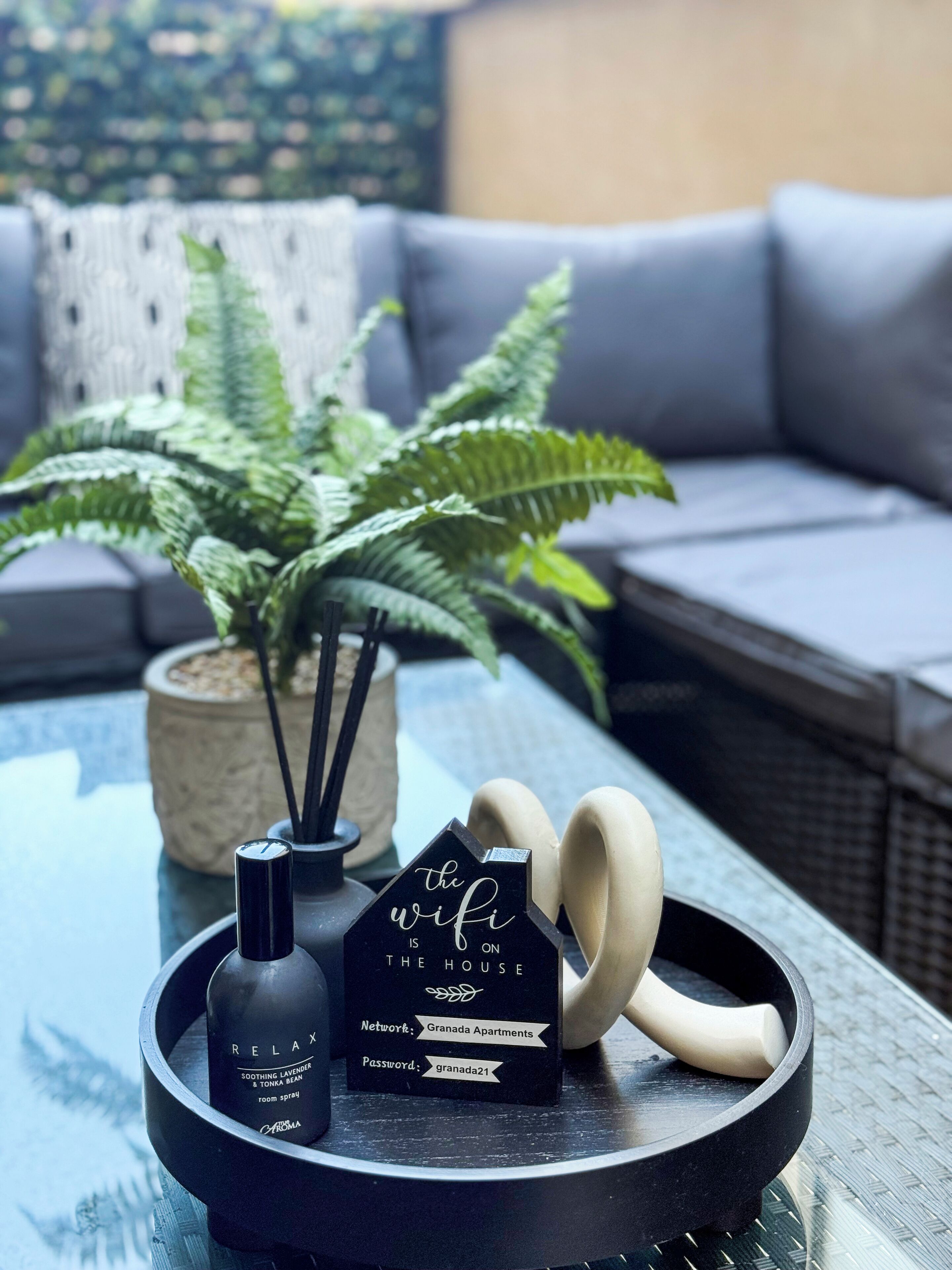 Une table en verre sur laquelle se trouve un plateau noir, un flacon de désodorisant d’intérieur, une boîte noire contenant des informations sur le réseau Wi-Fi et une paire d’écouteurs.