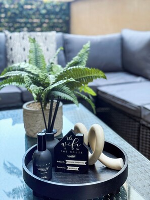 A glass table with a black tray holding a bottle of room spray, a black box with wifi information, and a pair of earphones. - Granada Apartments Queen's Promenade (Blackpool)