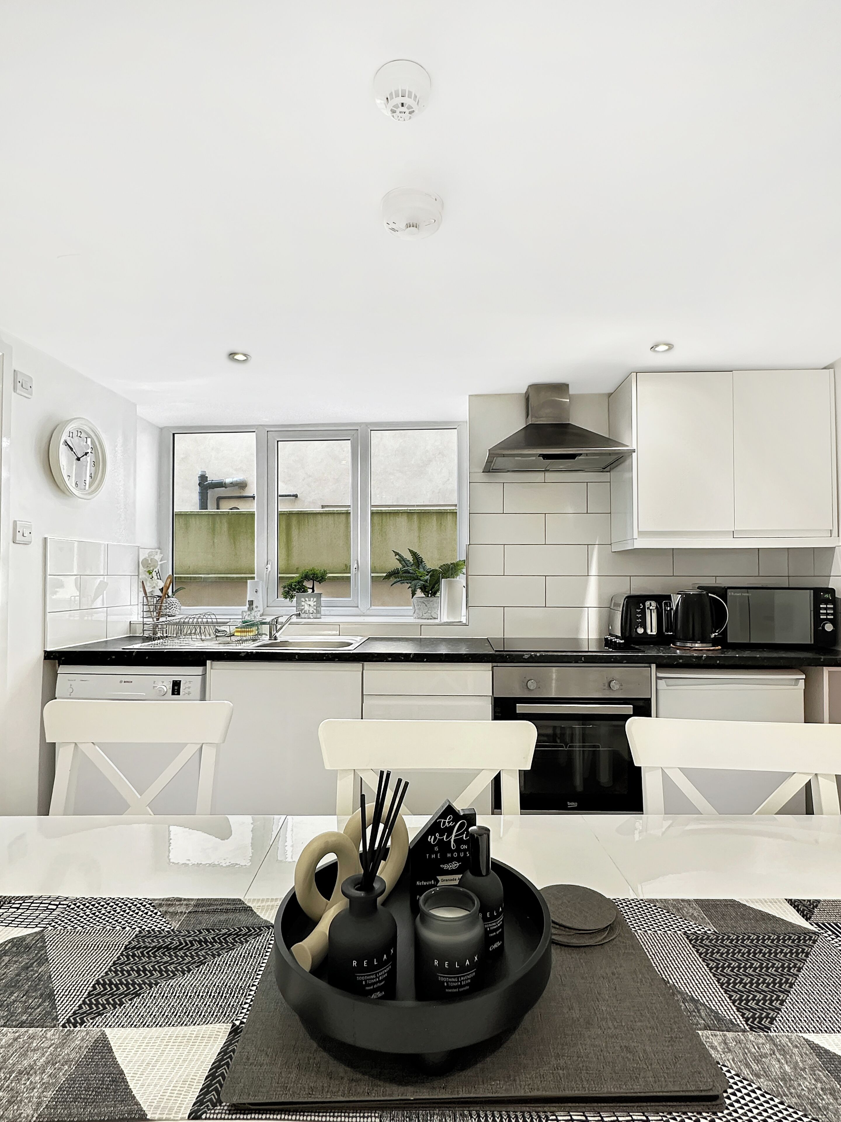 A modern kitchen with white cabinetry, a black countertop, and a dining area with a black and white patterned tablecloth.