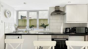 A modern kitchen with white cabinetry, a black countertop, and a dining area with a black and white patterned tablecloth.
