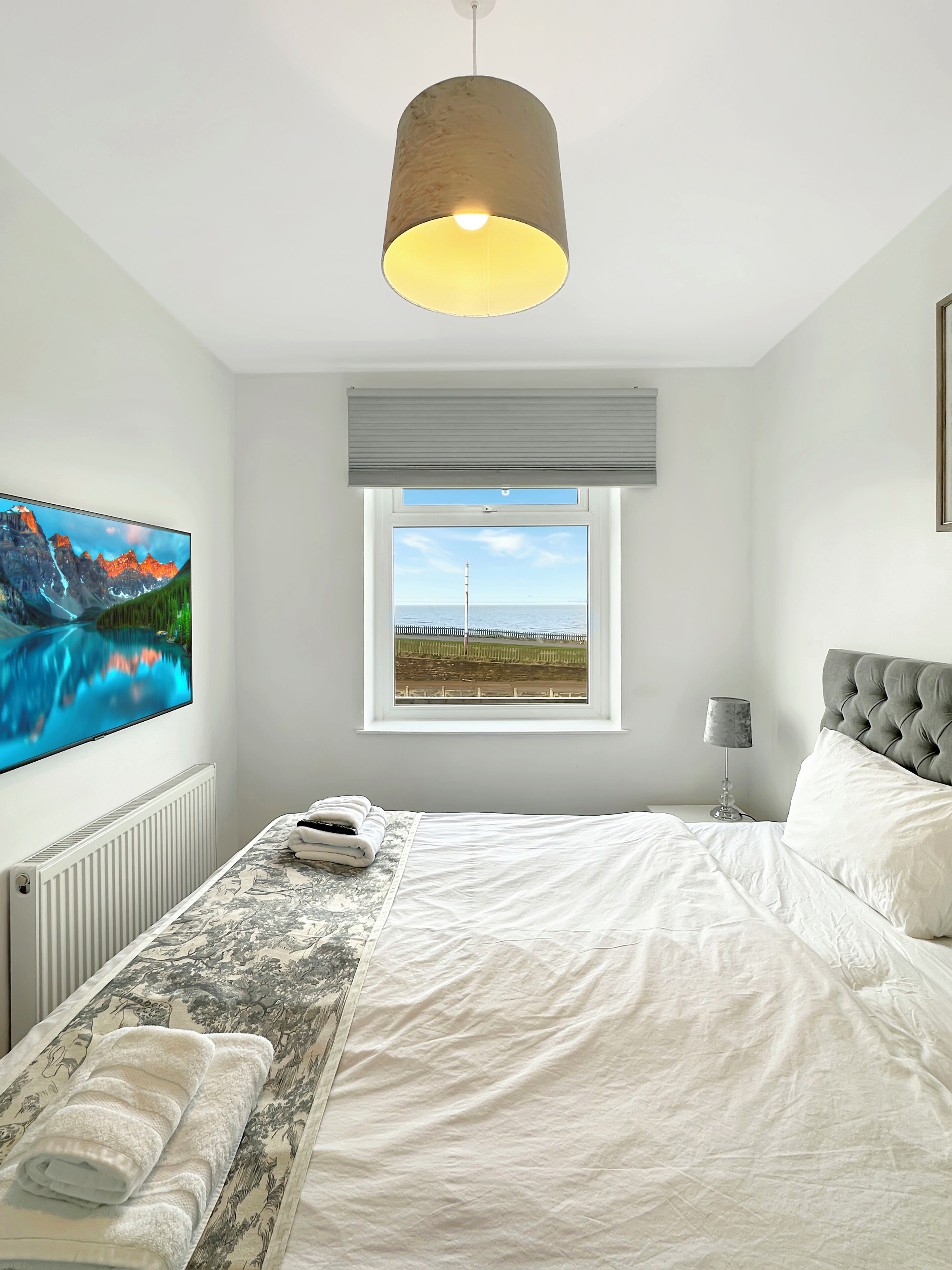 Ein Schlafzimmer mit Bett, Fenster mit Blick, einem Flachbildfernseher und einer Lampe.