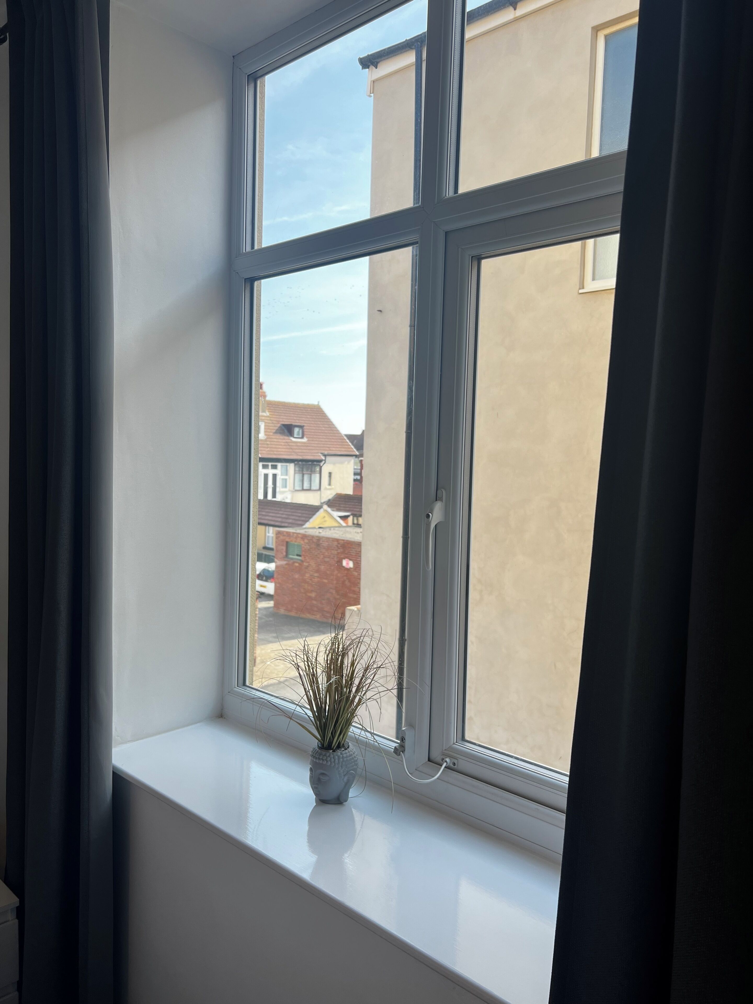 Una ventana con vistas a casas vecinas y una pequeña estatua de Buda en el alféizar.