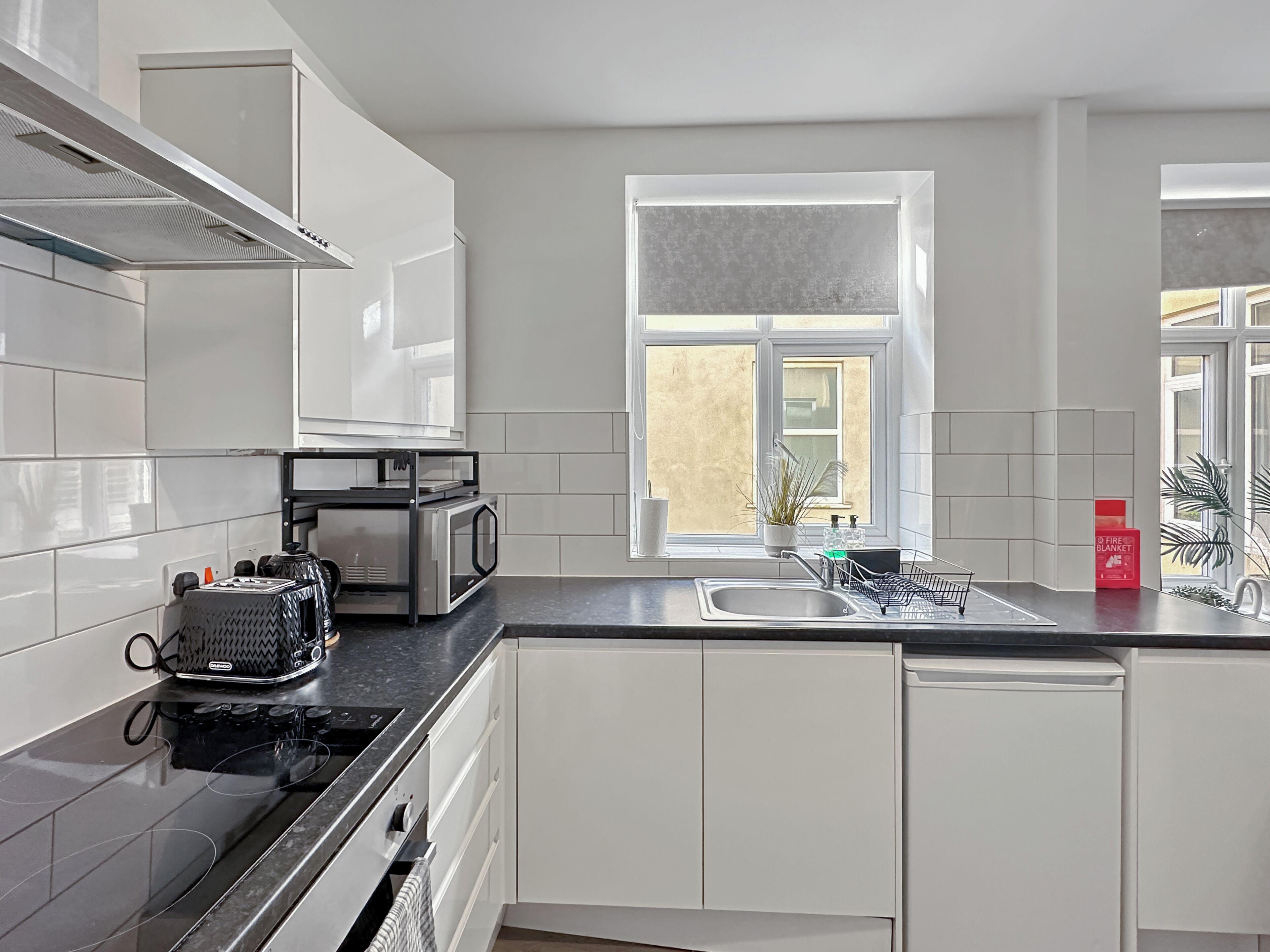 Una cocina moderna con armarios blancos, encimera negra, estufa, microondas y ventana con vistas.