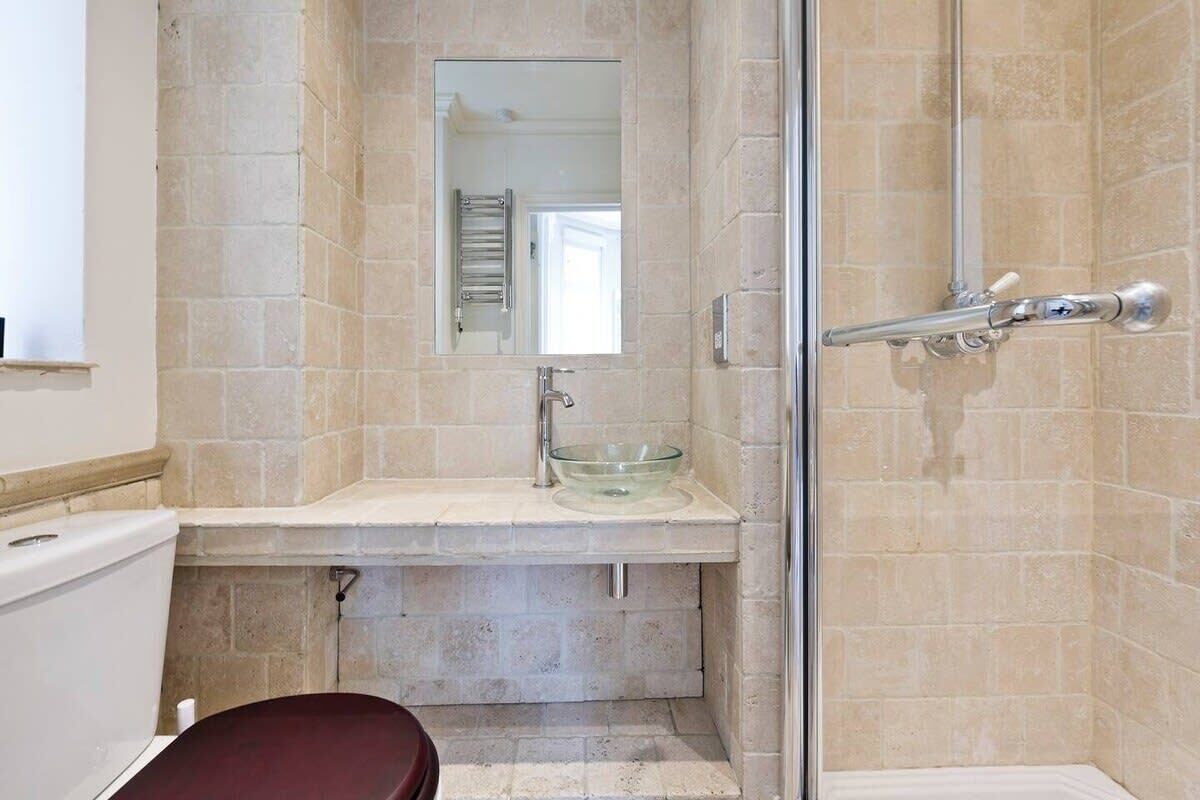 Een badkamer met een glazen douchecabine, een wastafel met een glazen wasbak en een toilet.