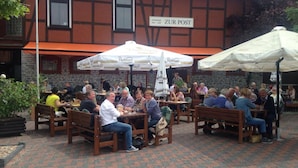 An outdoor café with wooden tables and benches, surrounded by a stone building with a sign reading "ZUR POST". - Gästehaus zur Post (Wabern)
