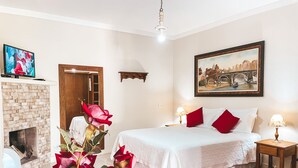 Un dormitorio con cama, chimenea, un cuadro y televisor en la pared.