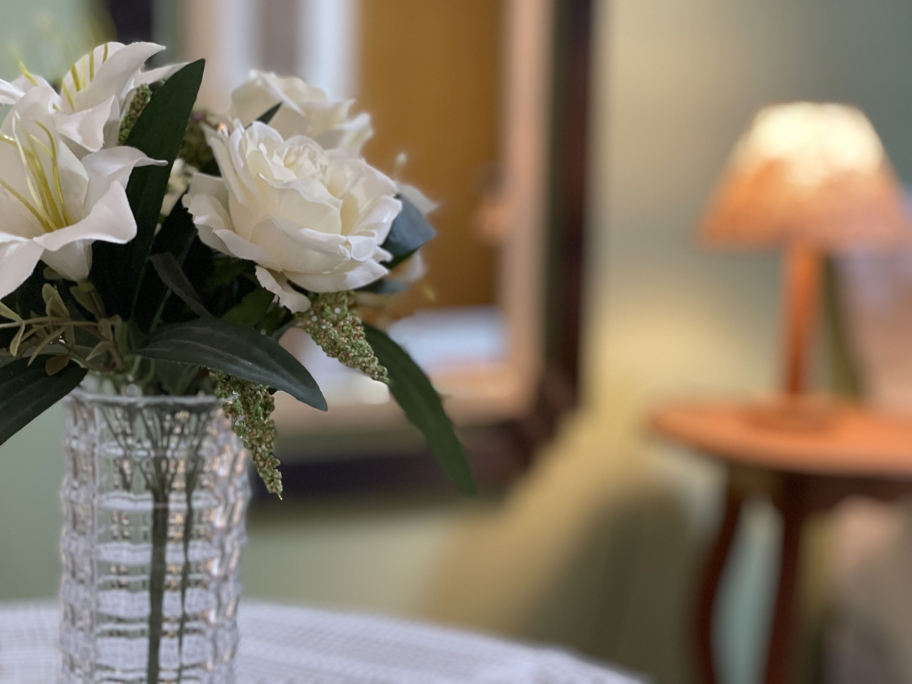 A clear glass vase with white flowers and green leaves on a table.