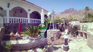 A courtyard with a white building featuring arches, a windmill, and a cactus garden. - CASA BELINDA - Savor nature (La Aldea de San Nicolás)
