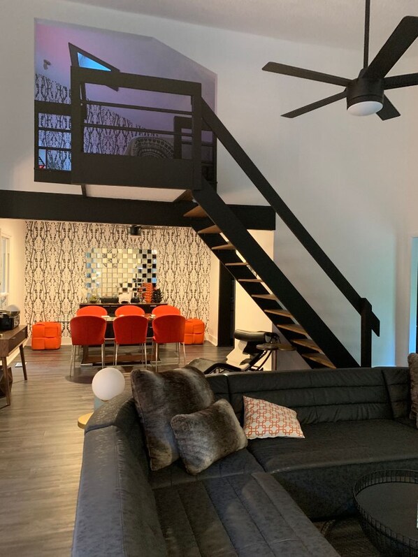 A modern living room with a black staircase, a dining area with red chairs, and a ceiling fan.