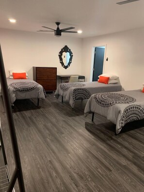 A room with three beds, a desk, a dresser, and a ceiling fan.