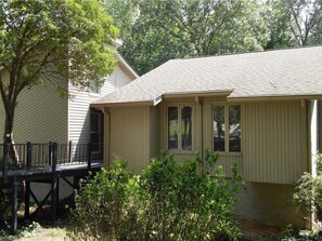 A single-story house with a front porch, a covered deck, and a small front yard with bushes.
