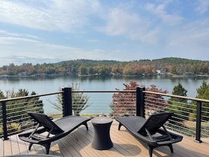 Terraza con dos sillones reclinables y una mesita, con vistas a un lago bordeado por un bosque.