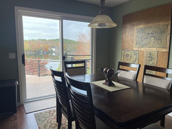 Un comedor con una mesa, sillas, un centro de mesa decorativo y vistas a un lago y árboles a través de un ventanal grande.