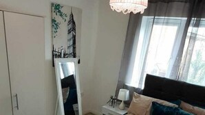 A bedroom with a bed, a bedside table, a lamp, a window, and a painting on the wall. - Lakeside Palace (Grays)