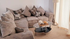 A living room with a beige sofa, multiple cushions, a glass coffee table with a tray of snacks, and a lamp. - Lakeside Palace (Grays)
