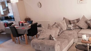 A cozy living room with a sofa, a dining table with chairs, and a glass coffee table. - Lakeside Palace (Grays)