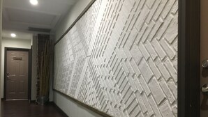Un pasillo con pared texturizada, una puerta de madera y un bote de basura metálico.