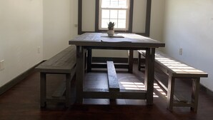 Una habitación con una gran mesa de madera, bancos, una planta en maceta y una ventana con persianas.