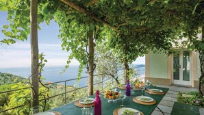 An outdoor dining table set with plates, cutlery, and glasses, surrounded by greenery and overlooking a scenic view. - S. Rocco dimora tra ulivi e M. (Zoagli)