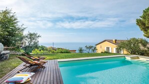 A swimming pool with wooden deck chairs and a colorful cushion, surrounded by greenery and a view of the sea. - S. Rocco dimora tra ulivi e M. (Zoagli)