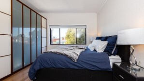A bedroom with a bed, a nightstand, a lamp, and a wardrobe. - Lighthouse Cozy 2BDR with CITY VIEWS (Middle Park)