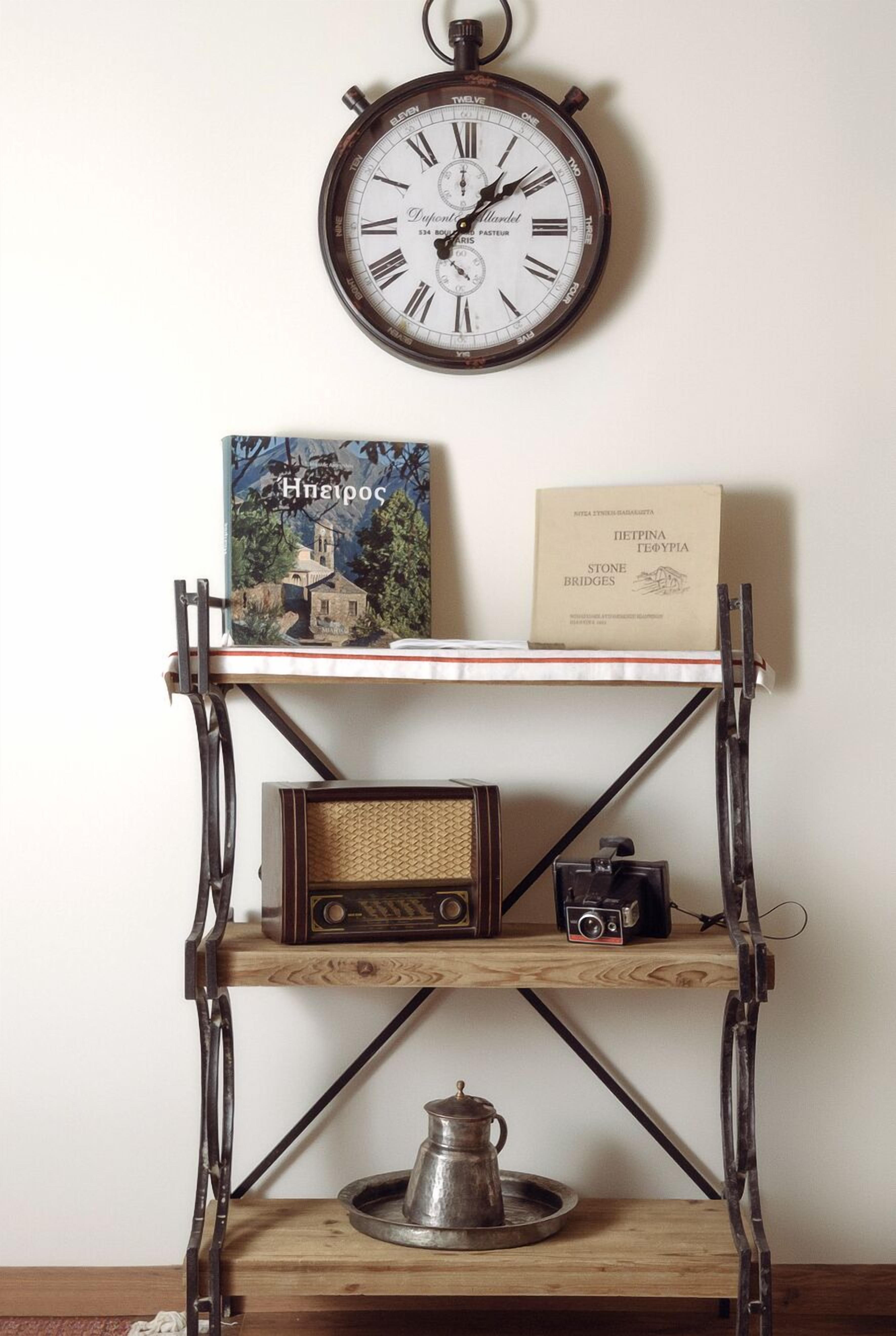 Un reloj de pared, un libro titulado 'Stone Bridges', una radio antigua y una cafetera de metal sobre un estante de madera.