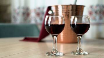 Dois copos de vinho tinto sobre uma mesa de madeira, com uma panela de cobre ao fundo.