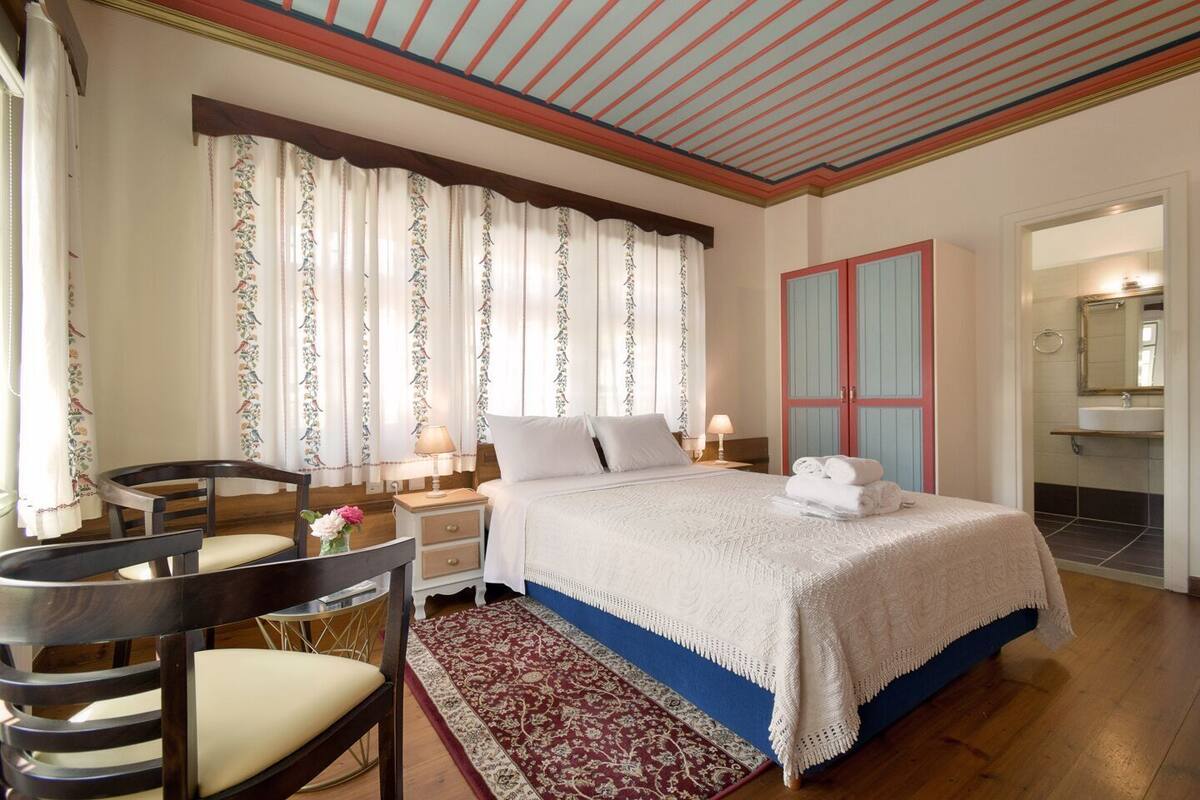 Ein Hotelzimmer mit Bett, Schreibtisch mit Stuhl, Badezimmer mit Waschbecken und Spiegel sowie Kleiderschrank mit zwei Türen.