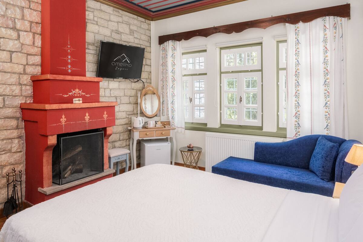Ein Zimmer mit Kamin, einem Bett, einem blauen Sofa und einem Fenster mit Vorhängen.