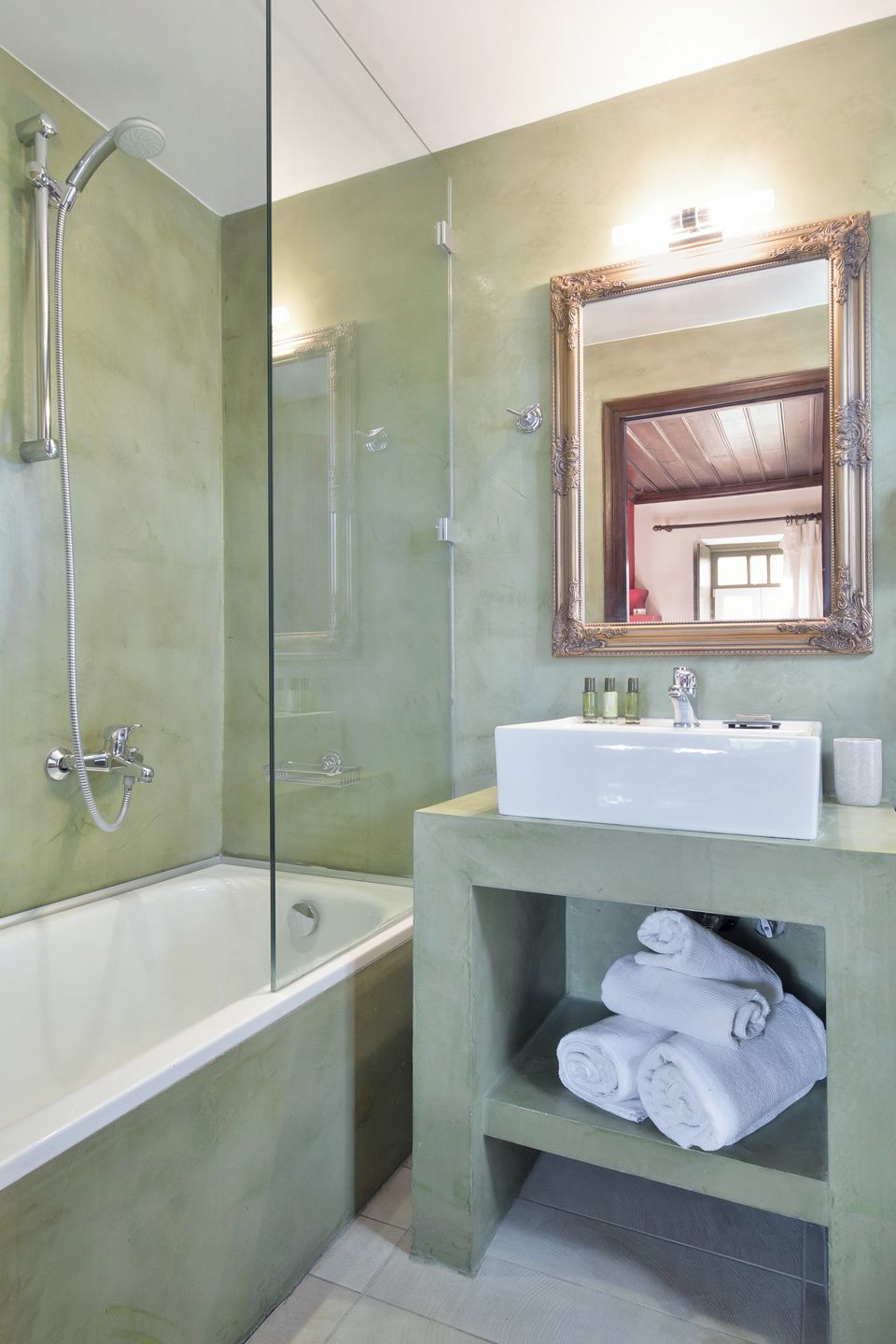 A bathroom with a bathtub, a shower, a sink with a mirror, and a shelf with towels.