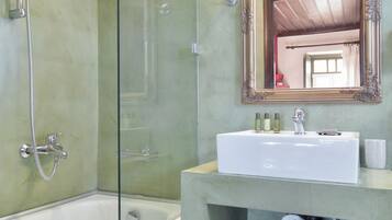 A bathroom with a bathtub, a shower, a sink with a mirror, and a shelf with towels.