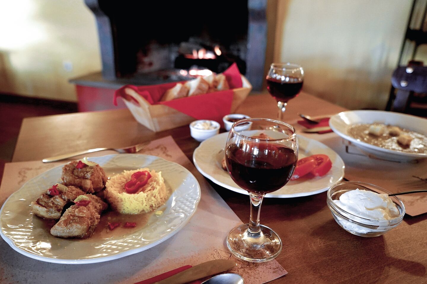 A dining table with plates of food, a glass of red wine, and a small bowl of cream.